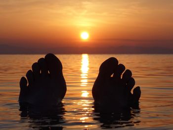 Silhouette hand in sea against sky during sunset