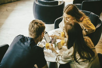 High angle view of friends using smart phone while having drinks in restaurant