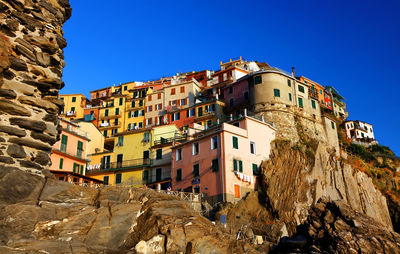 Low angle view of residential buildings on rocky mountain against clear blue sky