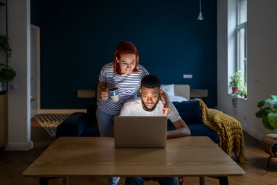 Loving woman wife standing behind husband working on laptop, supporting him in online business