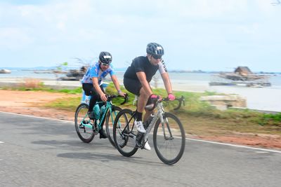 People riding bicycle on sea shore against sky