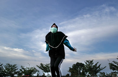 Low angle view of woman wearing mask against sky