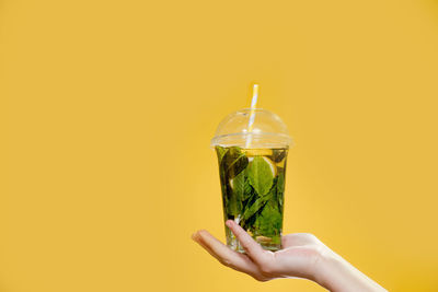 Close-up of hand holding drink against yellow background