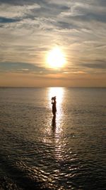 Silhouette man standing on sea against sky during sunset