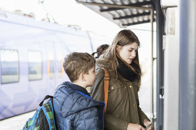 Boy looking at sister buying tickets from automated machine at train station