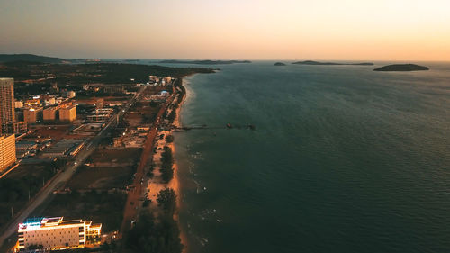 High angle view of illuminated city by sea against sky at sunset