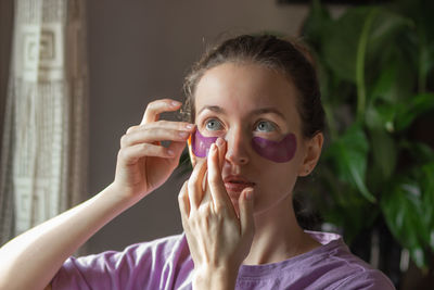 Young woman applying purple hydrogel eye patches against wrinkles, puffiness and dark circles.