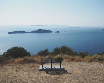 Bench on shore by sea against clear sky