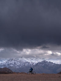 Man with bicycle against mountains and stormy clouds during winter