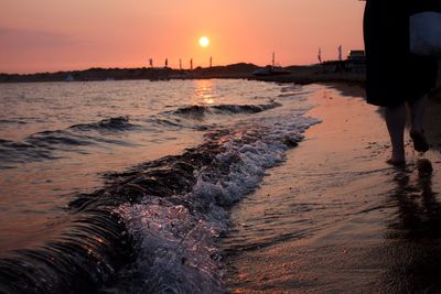 Rear view of woman walking at beach during sunset