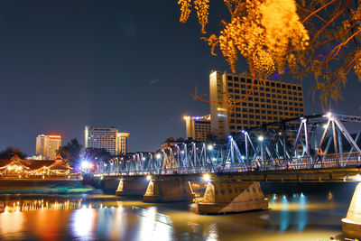 Illuminated buildings by river against sky at night