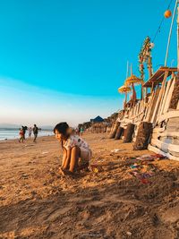 Girl playing with sand at beach against clear blue sky