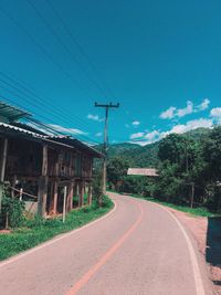 Road by buildings against blue sky