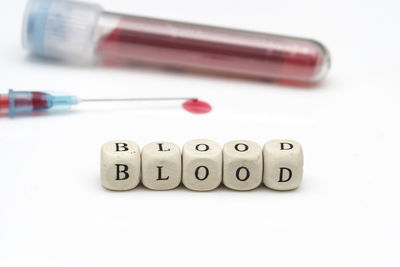 Close-up of toy blocks with text by syringe with blood against white background