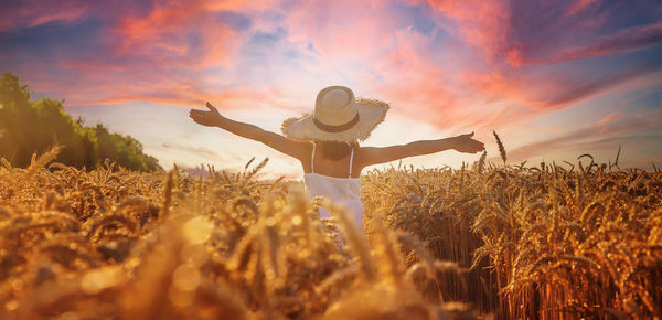 Rear view of woman standing on field against sky during sunset