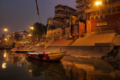 Boats moored on canal by illuminated buildings in city at night