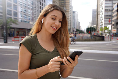 Smiling stylish girl reading a text message on her phone while commuting in the city