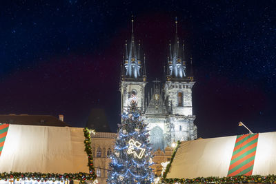 Illuminated christmas tree by building against sky at night