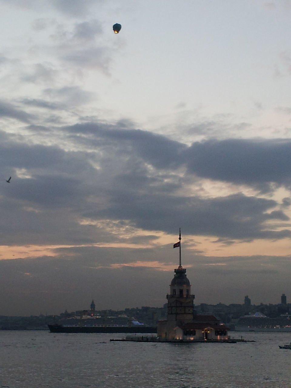 building exterior, architecture, built structure, sky, sunset, city, cloud - sky, bird, water, transportation, silhouette, outdoors, flying, sea, crane - construction machinery, tower, nature, mode of transport, dusk, cloud