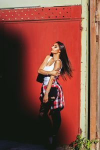 Young woman standing against red wall