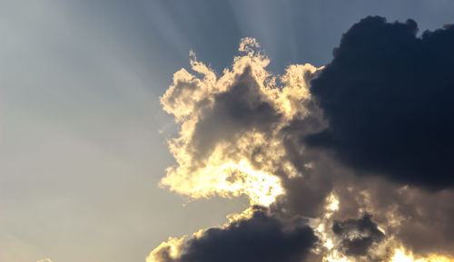 Low angle view of sunlight streaming through clouds