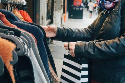 Midsection of woman choosing from clothes rack at street market in city