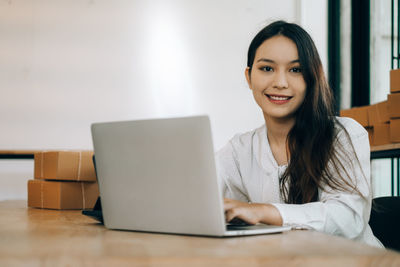 Portrait of smiling young woman using phone while sitting on table