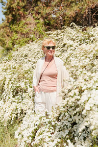 Elderly woman posing among bushes with white flowers