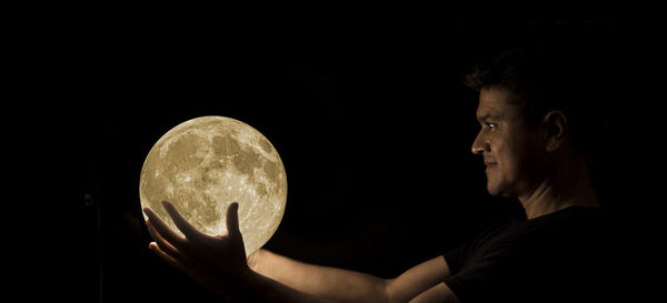 Man holding moon shape illuminated light against black background