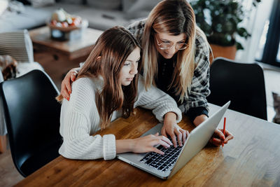 High angle view of mother by daughter using laptop on table