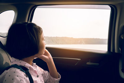 Girl looking through window while sitting in car
