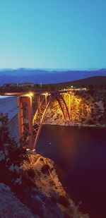 Illuminated bridge over river against clear sky at night