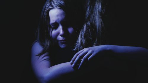 Close-up of depressed woman crying by holding friend against black background