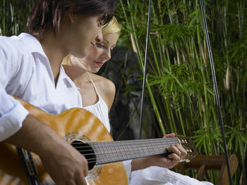 Boyfriend playing guitar while sitting with girlfriend on swing at resort