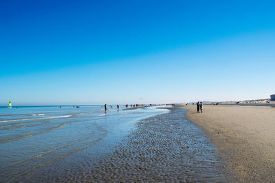 People on beach against clear blue sky
