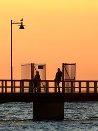 Silhouette people standing by sea against clear sky during sunset
