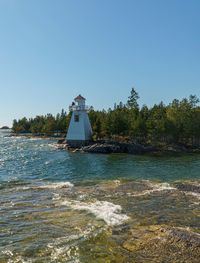 Lighthouse by sea against clear sky