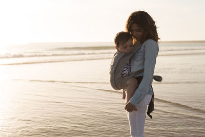 Mother carrying son while standing at beach