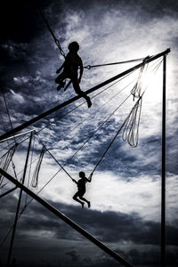 Low angle view of silhouette man hanging on rope against sky