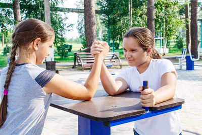 Friends playing arm wrestling on table in park