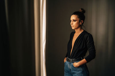 Woman looking away while standing against wall