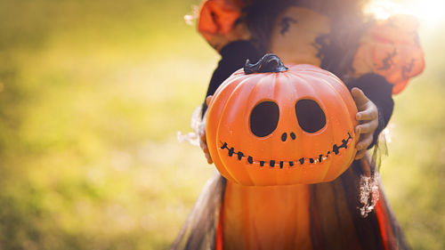 Pumpkin head jack-o'-lantern in the hands of a girl in a witch costume 