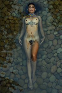 High angle view of young naked woman lying on pebbles in shallow water