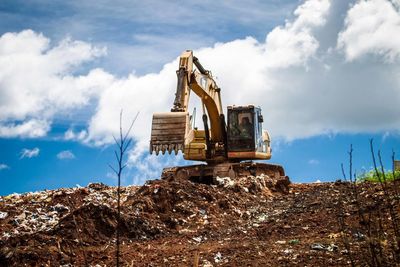 Earth mover on land against cloudy sky