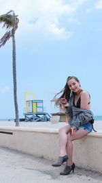 Full length of happy woman sitting on the boardwalk with a donut 