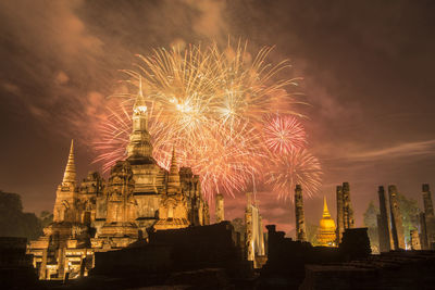 Firework display over illuminated building against sky at night