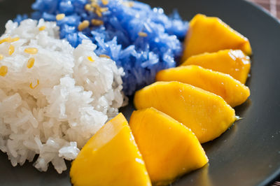 Close-up of white and blue rice with mango served in plate