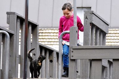 Full length of girl by tortoiseshell cat on wooden play equipment