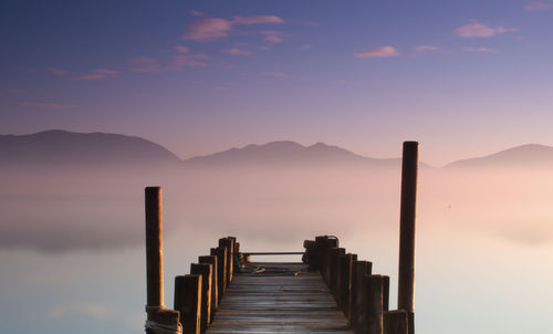 Wooden posts on pier against sky during sunrise