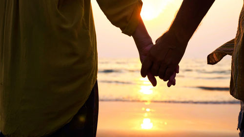 Midsection of man holding hands against sky during sunset